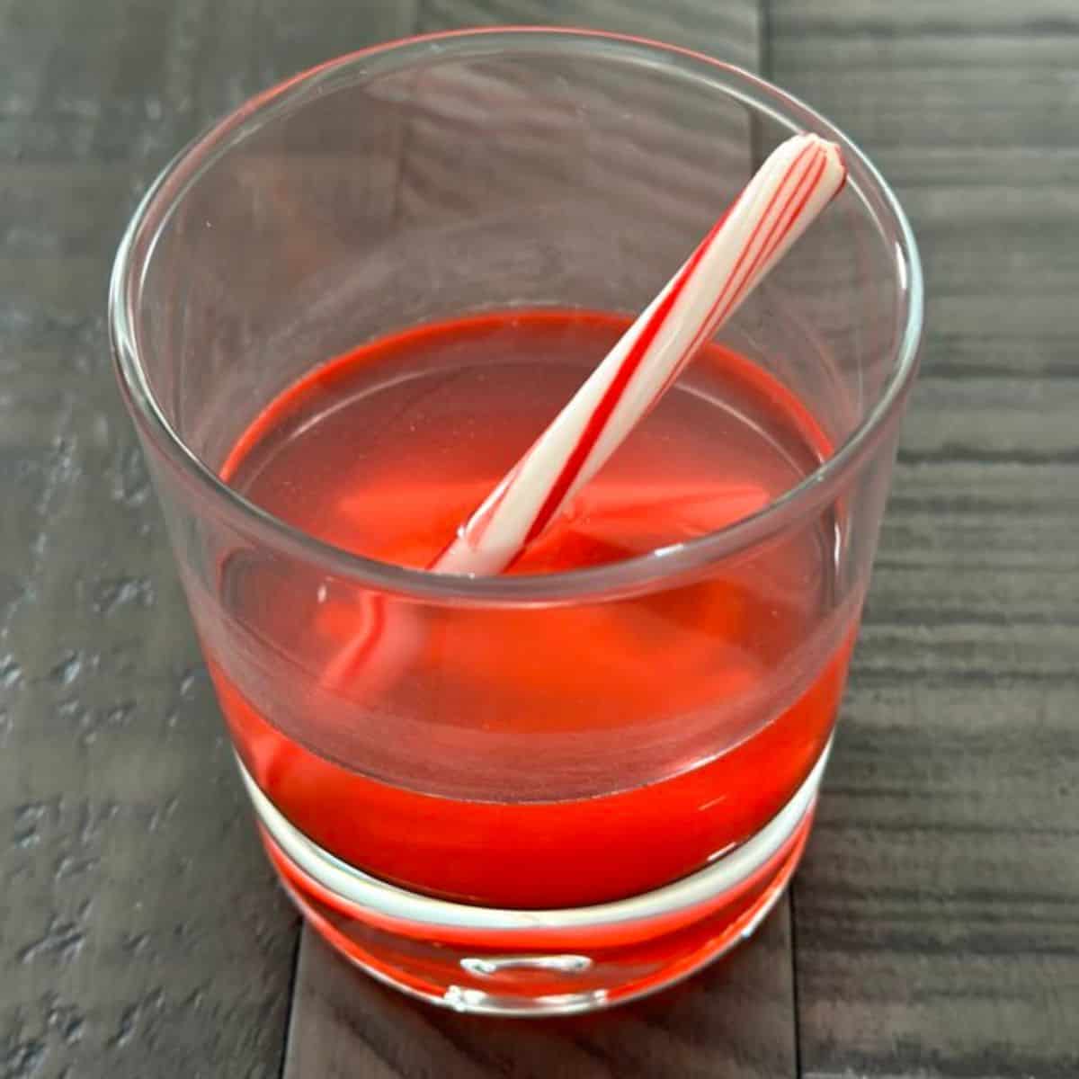 Old fashioned glass with a candy cane slowly melting in vodka.
