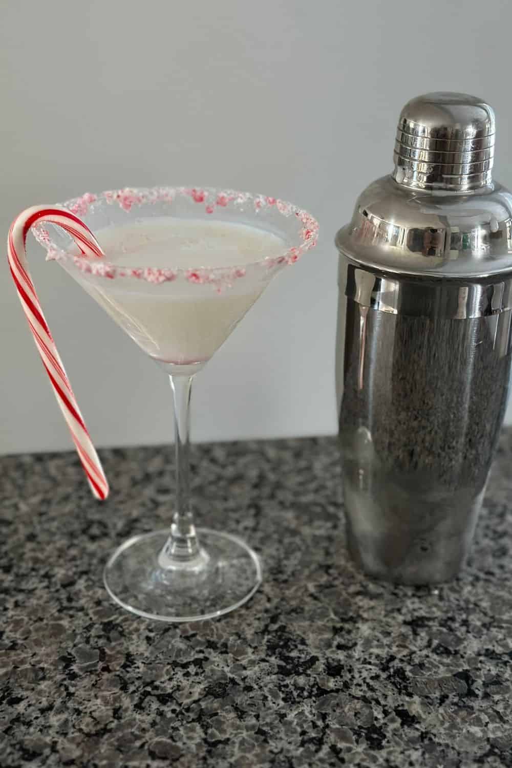 A candy cane martini sitting on a counter next to a cocktail shaker.